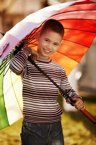 Happy boy with a rainbow umbrella in park — Stock Photo, Image