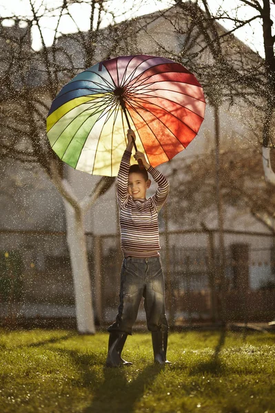 Menino feliz com um guarda-chuva arco-íris no parque — Fotografia de Stock