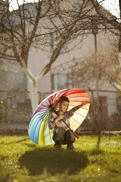 Niño feliz con un paraguas de arco iris en el parque — Foto de Stock