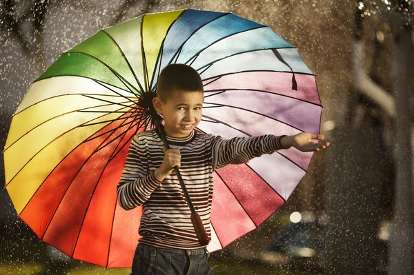 Happy boy with a rainbow umbrella in park — Stock Photo, Image