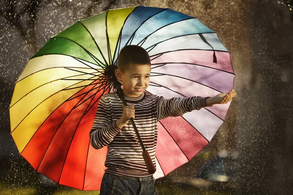 Lycklig pojke med en regnbåge paraply i park — Stockfoto