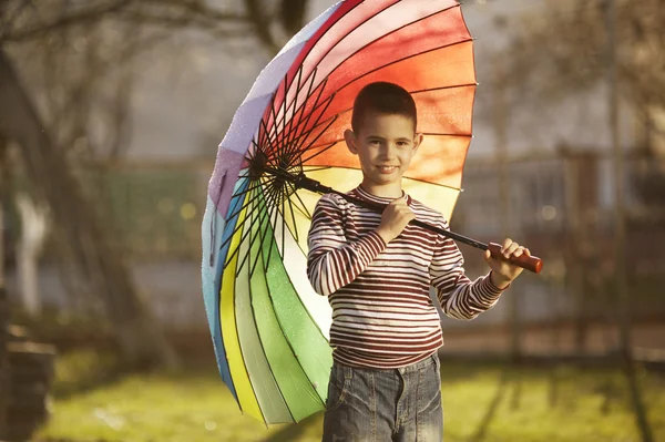 Menino feliz com um guarda-chuva arco-íris no parque — Fotografia de Stock