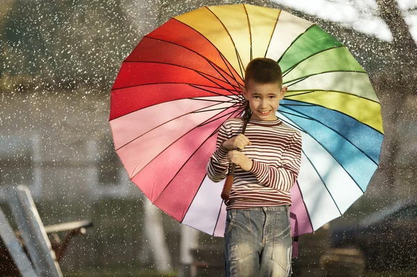 Happy boy with a rainbow umbrella in park — Stock Photo, Image