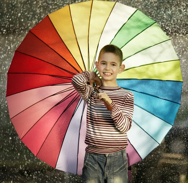 Happy boy with a rainbow umbrella in park — Stock Photo, Image