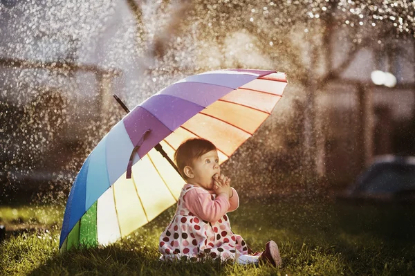Little girl with a rainbow umbrella in park — Stock Photo, Image