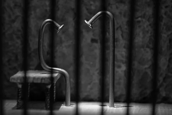 Conceptual jail photo with iron nail sitting behind bars artisti — Stock Photo, Image