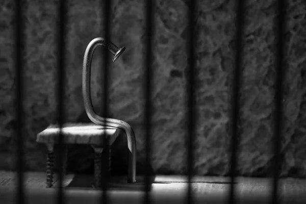 Conceptual jail photo with iron nail sitting behind bars artisti — Stock Photo, Image