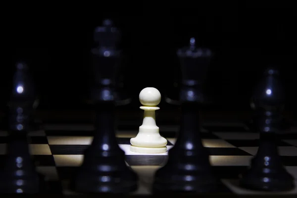 White pawn standing alone in spotlight on chess board with black — Stock Photo, Image