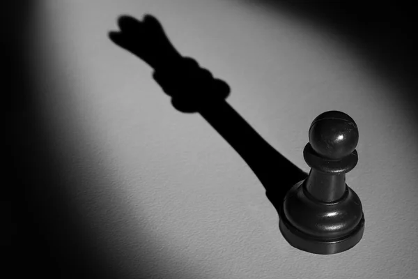 Chess pawn staande in een middelpunt van de belangstelling die een schaduw van koningin maken een — Stockfoto