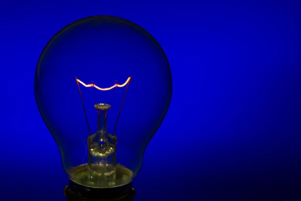 Glass light bulb with burning filament upright with blue backgro — Stock Photo, Image