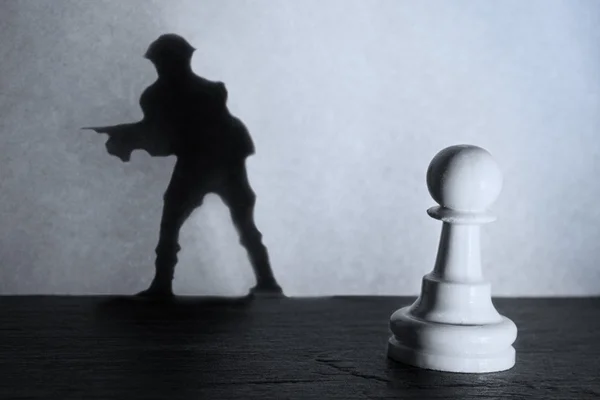 Chess pawn standing in a spotlight that make a shadow of soldier — Stock Photo, Image