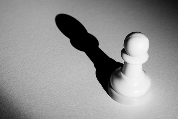 Peão de xadrez em pé em um holofote que faz uma sombra — Fotografia de Stock