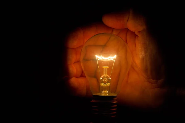 闇のエネルギーを節約するために電球を保持している人間の手 — ストック写真