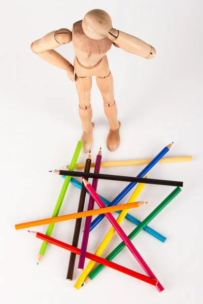Mannequin en bois confus debout au tas de crayon de couleur isolat — Photo