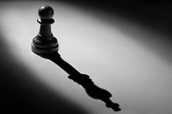 Chess pawn standing in a spotlight that make a shadow of king