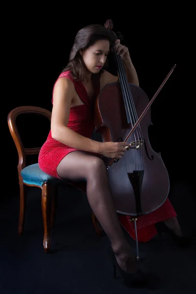 Hermosa morena tocando el violonchelo con luz selectiva en rojo dre — Foto de Stock