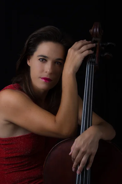 Beautiful brunette holding cello with selective light in red dre — Stock Photo, Image