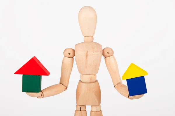 Small wood mannequin sit holding colourful block house isolated — Stock Photo, Image