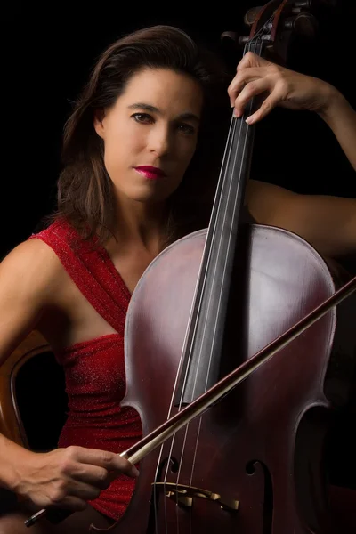 Belle brune jouant du violoncelle avec lumière sélective en dre rouge — Photo