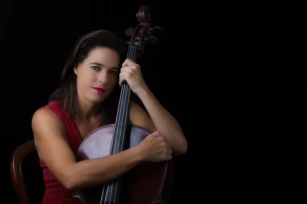 Cantik brunette memegang cello dengan cahaya selektif di merah dre — Stok Foto
