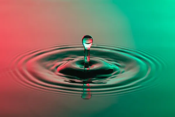 Gota de água perto com ondulações concêntricas vermelho colorido e gr — Fotografia de Stock