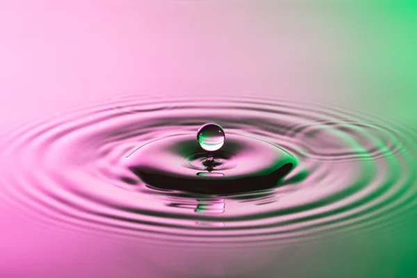 Gota de agua de cerca con ondas concéntricas de color rosa y g —  Fotos de Stock