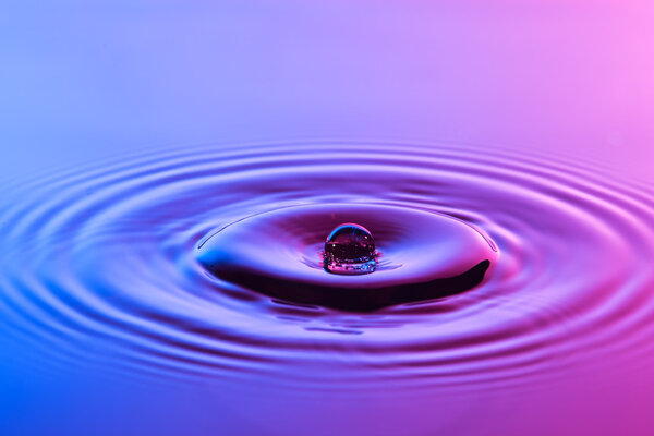 Капля воды близко с концентрической рябью красочный синий и р
