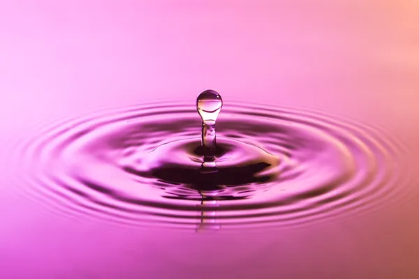 Gota de agua de cerca con ondas concéntricas de color rosa e y —  Fotos de Stock
