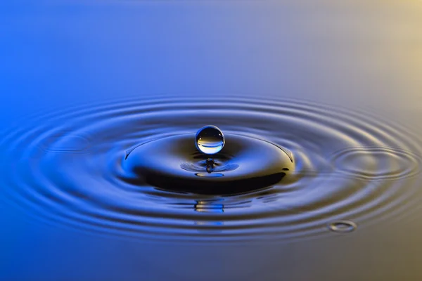 Goccia d'acqua da vicino con increspature concentriche colorate blu e y — Foto Stock