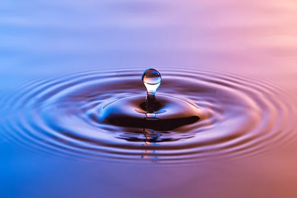 Kapka vody blízko se soustředným vlnky barevné modré a — Stock fotografie
