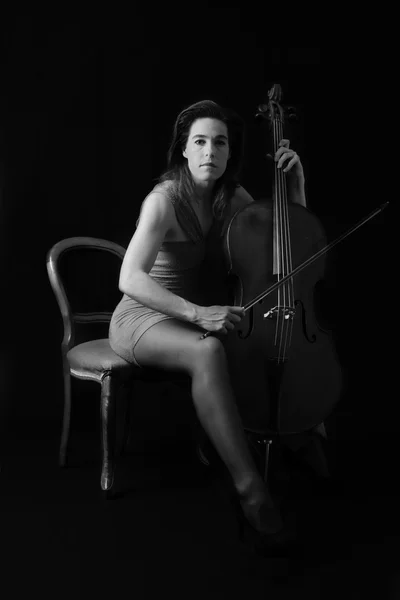 Belle brune jouant un violoncelle avec lumière sélective en noir — Photo