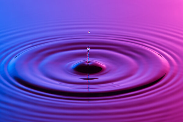 Капля воды близко с концентрической рябью красочный синий и р
