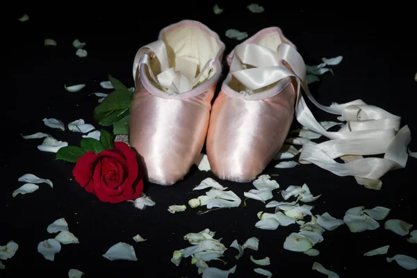 Old used ballet slippers lying on floor with rose and petal — Stock Photo, Image