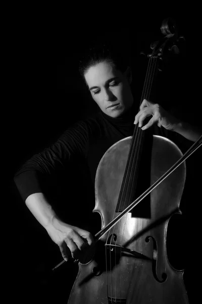 Linda morena tocando um violoncelo com luz seletiva em preto — Fotografia de Stock