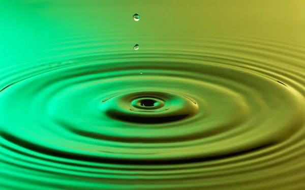 Waterdruppel dicht omhoog met concentrische rimpelingen kleurrijke groen en — Stockfoto