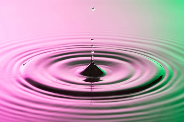 Gota de agua de cerca con ondas concéntricas en la superficie de color rosa y verde —  Fotos de Stock