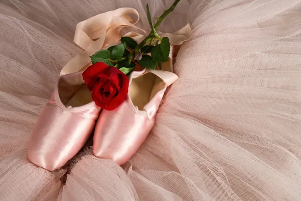 Old used ballet slippers lying on floor with rose and tutu — Stock Photo, Image