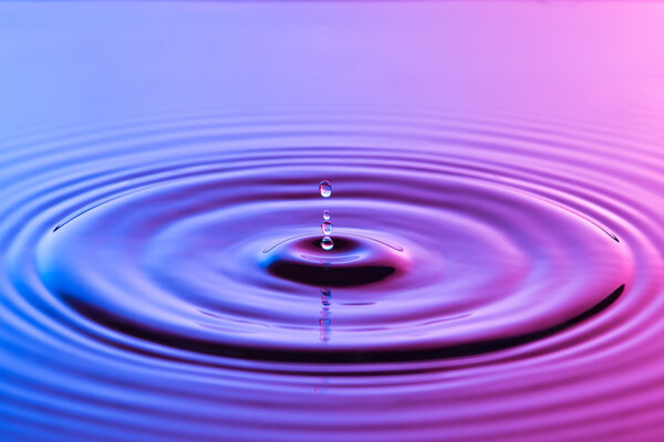 Капля воды близко с концентрической рябью красочный синий и р
