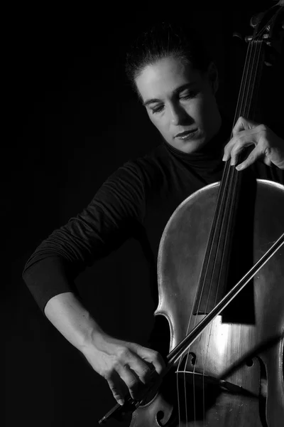 Linda morena tocando um violoncelo com luz seletiva em preto — Fotografia de Stock