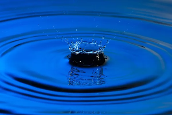 Kapka vody zblízka s soustředné kruhy barevné modré povrchovým vodám — Stock fotografie