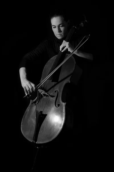 Belle brune jouant un violoncelle avec lumière sélective en noir — Photo