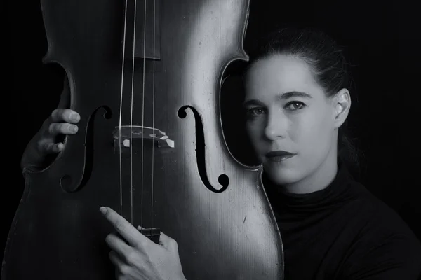 Beautiful brunette playing a cello with selective light in black — Stock Photo, Image