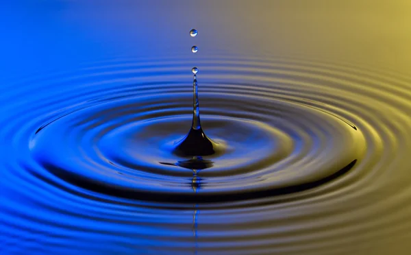 Goutte d'eau de près avec des ondulations concentriques coloré bleu et y — Photo