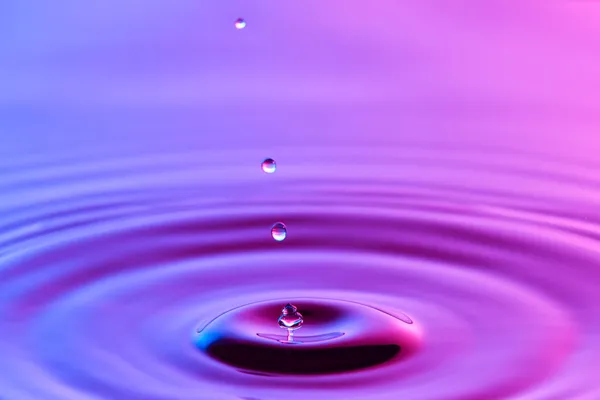 Падіння води крупним планом з концентричними пульсаціями барвистий синій і р — стокове фото