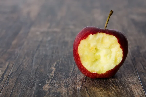 Rode appel met een gat erin gebeten op een bruine oppervlak — Stockfoto