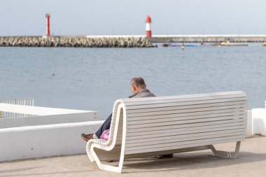 İnsanlar deniz manzaralı banklarda oturur..