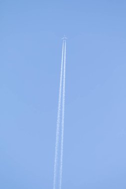 Mavi gökyüzü ve gökyüzünde yükselen uçak izleri.