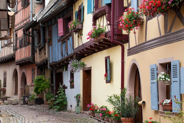 Calle con casas medievales de entramado de madera en el pueblo de Eguisheim a lo largo de la famosa ruta del vino en Alsacia, Francia — Foto de Stock