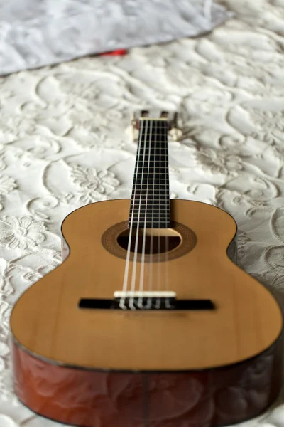 Španělská kytara leží na posteli — Stock fotografie