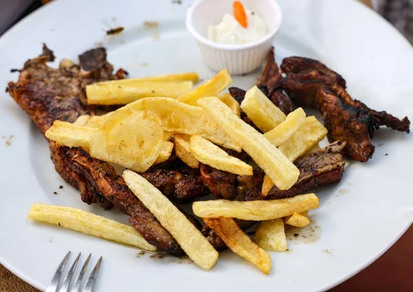 grilled goat with fries on a white plate